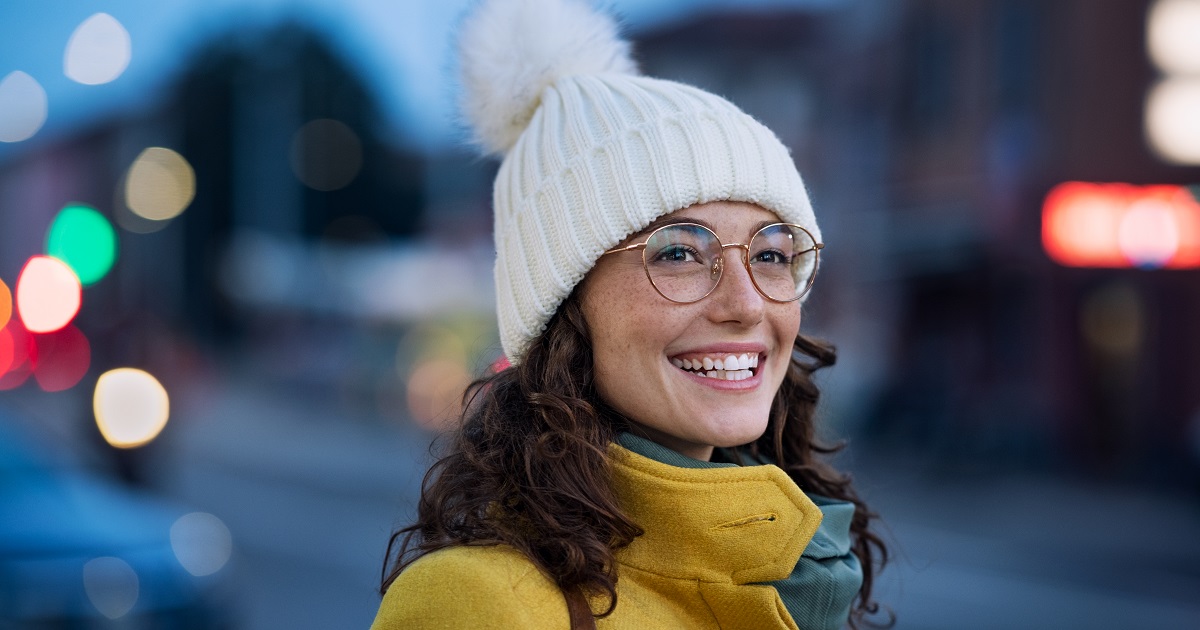 A young woman smiling in a winter hat and glasses. 