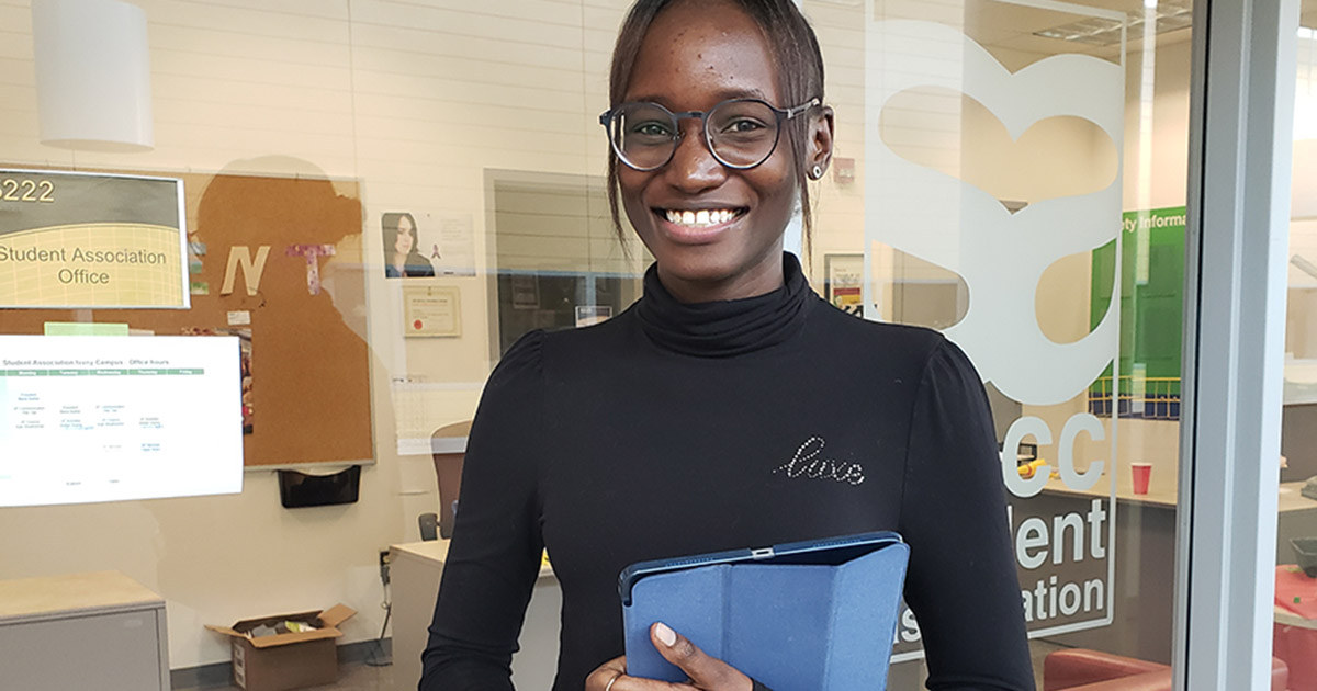 Ribi, a young woman from Kenya, stands in front of the glass walls of the NSCC Student Association offices.