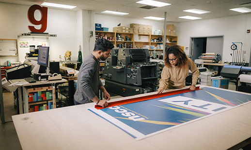 Two people working on a poster at a giant table in a production studio. 