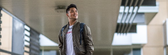 A student stands in front of NSCC Ivany Campuses main entrance and gazes over his left shoulder.