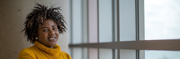 A student sits at a table near a window at NSCC Ivany Campus and smiles at the camera.