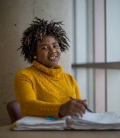 A student sits at a table near a window at NSCC Ivany Campus and smiles at the camera.