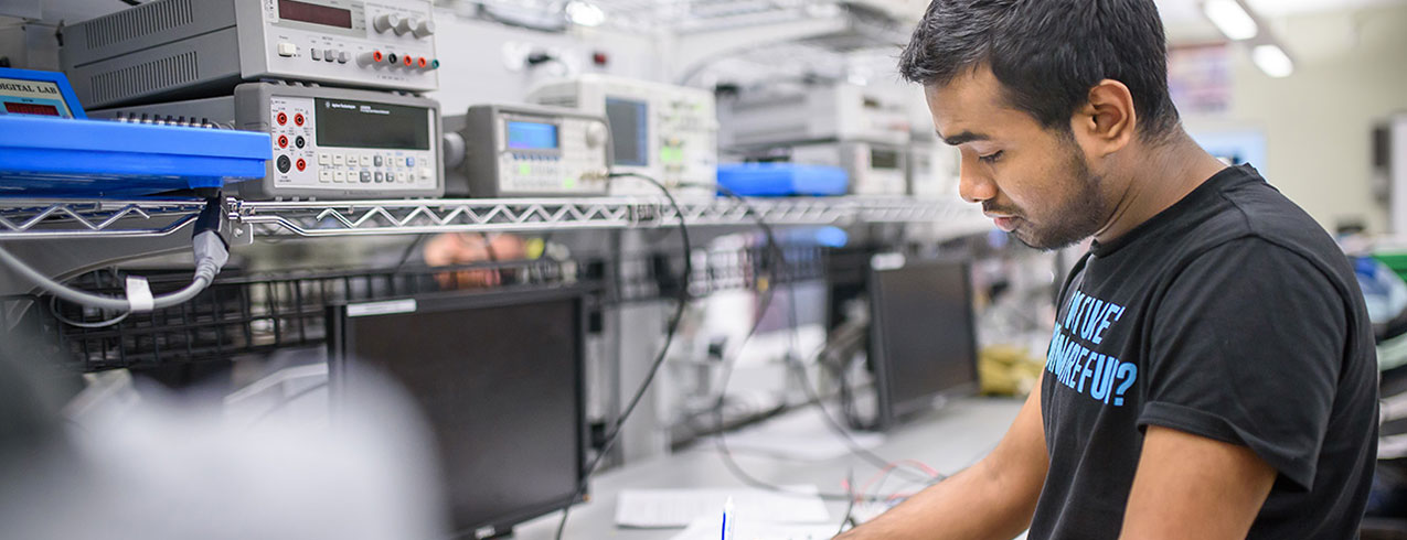 An Electronic Systems Technician student works on a piece of equipment in the workshop surrounded by electronics.