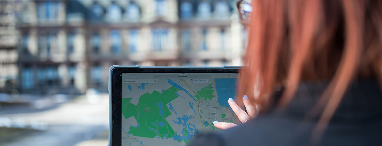A student in the Geographic Information Systems Technician program is seen from behind working on a computer showing a map.