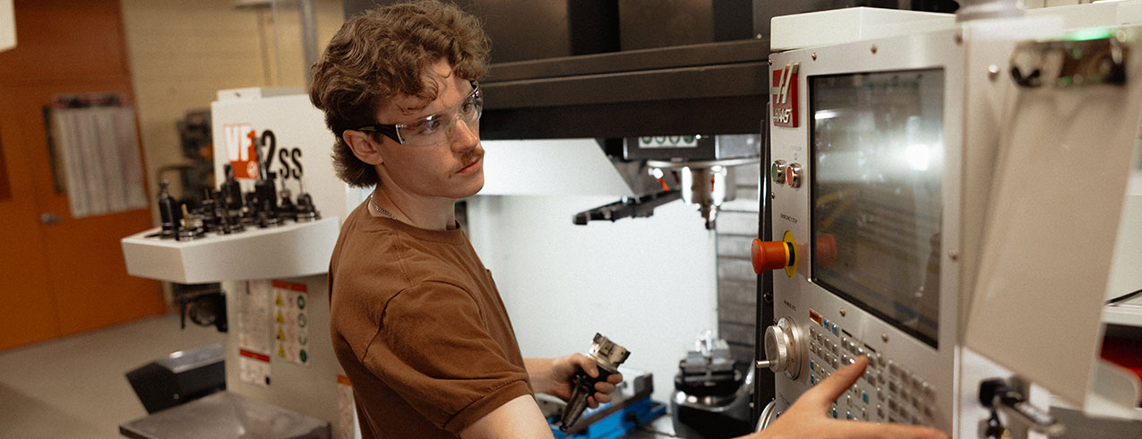 A student of the CNC Machining program, Ben Campbell is seen working on a machine in a workshop setting..