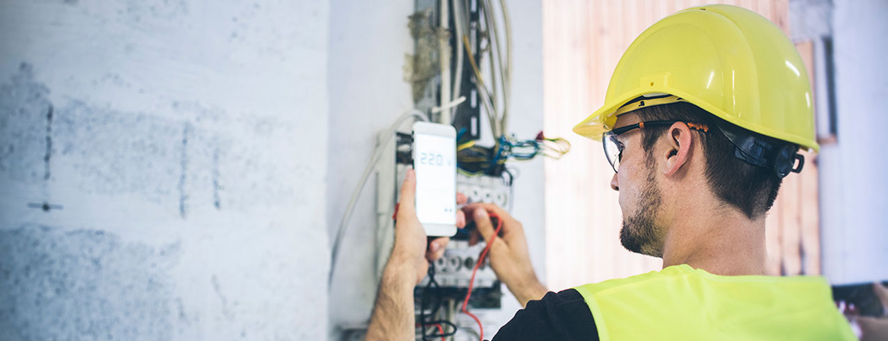 An Electrical-Industrial Maintenance and Controls student is seen in yellow hard hat and vest working on a machine. 