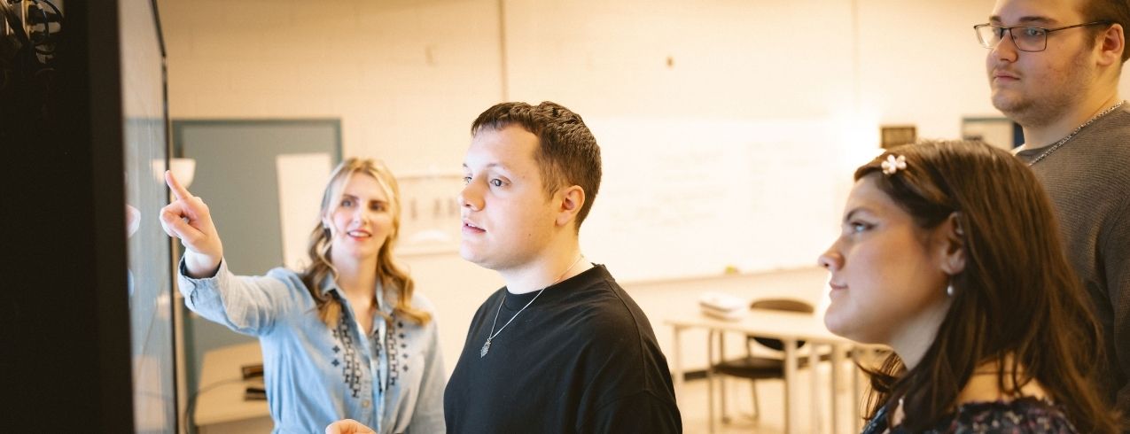 A group of NSCC Achieve students look at a whiteboard together with their instructor at an NSCC campus.