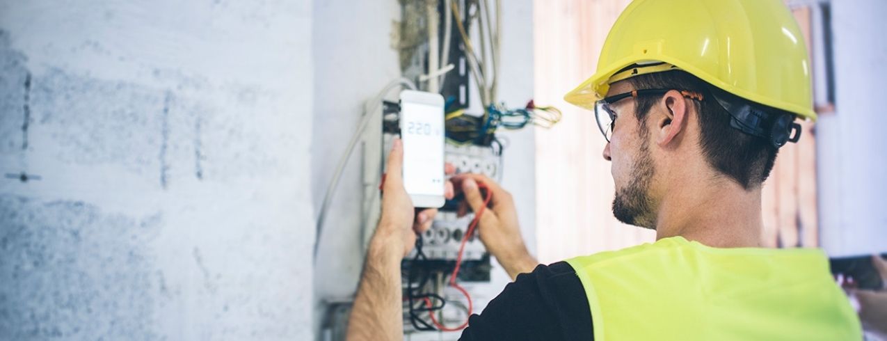 An electrical worker uses a device to measure activity in a an electrical control centre.