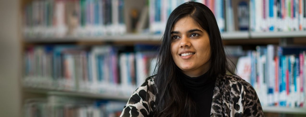 An NSCC international student sits and smiles in a library study space at an NSCC campus.