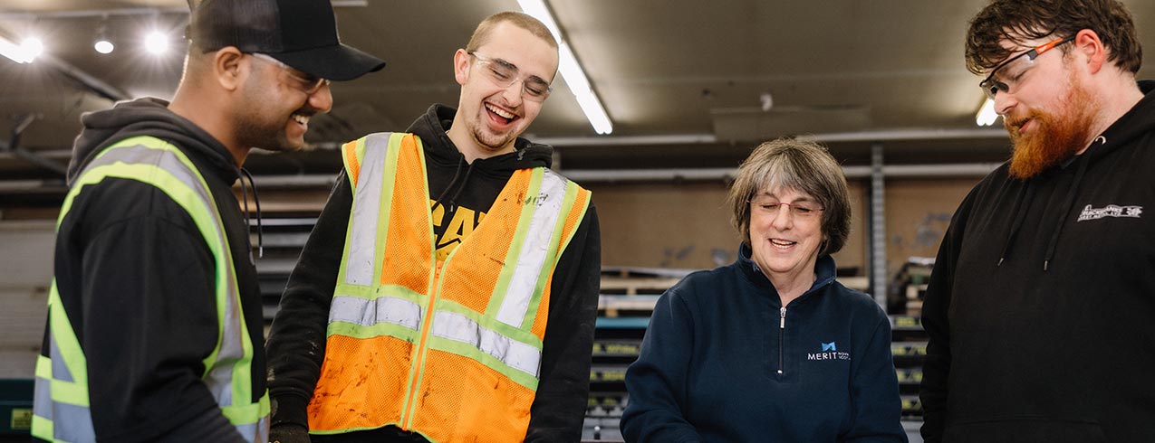 Three NSCC trades students stand with an NSCC instructor and learn in a shop setting.