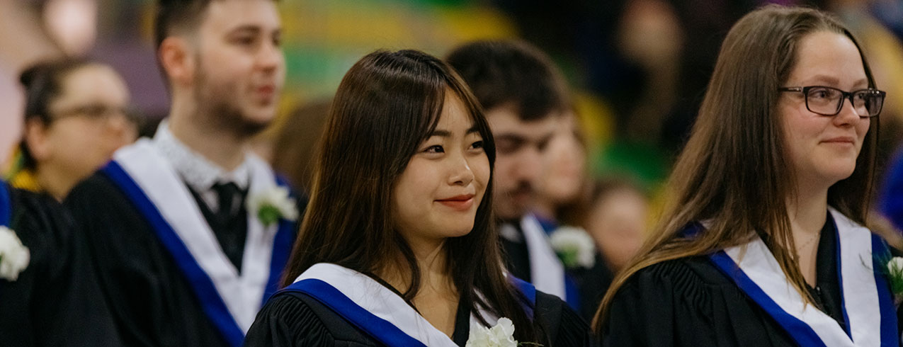 Two female graduates are seen smiling surrounded by their fellow graduates during Convocation ceremonies.