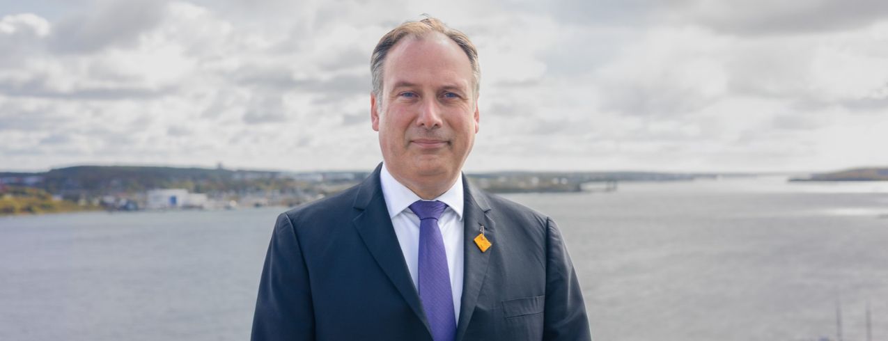 Image of David Benoit, NSCC's new President. He is standing in front of a body of water, wearing a navy suit.