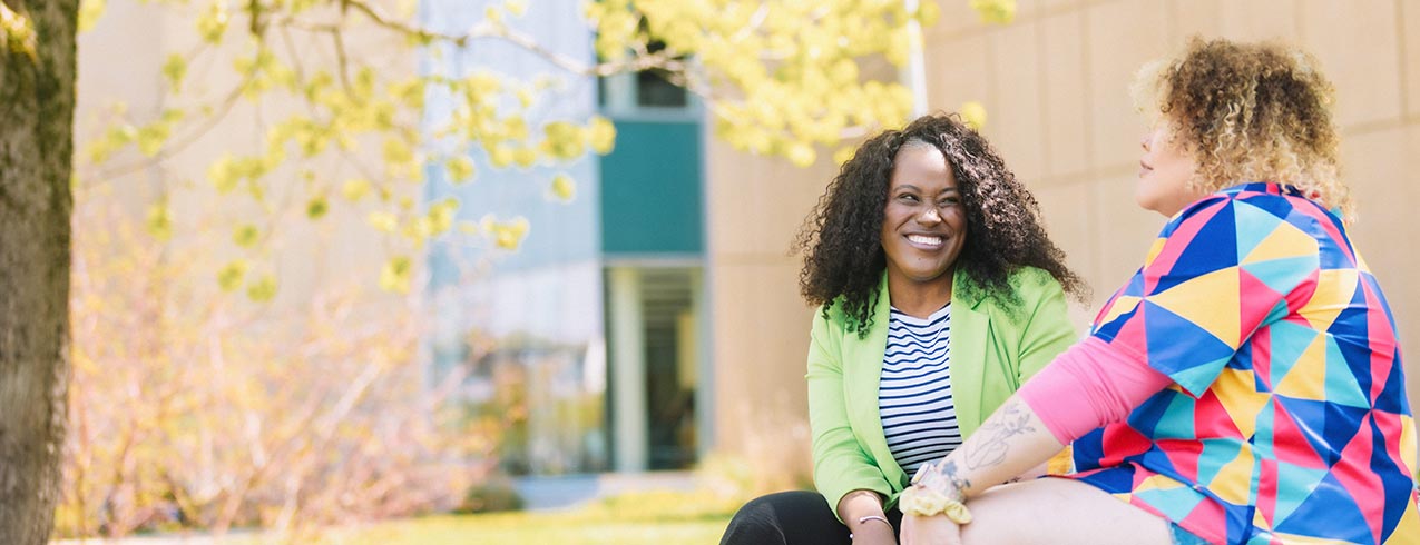 Two people sit outside in front on an NSCC campus while smiling and talking. The photo has a graphic on it that says NSCC Open House.