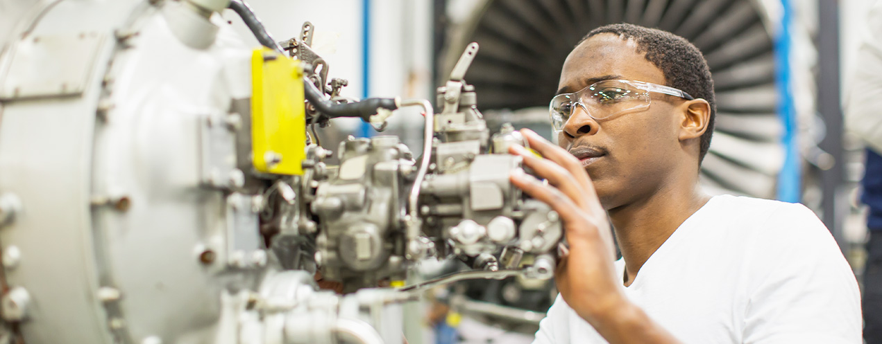 Daniel Kakonge, a student in the Aircraft Maintenance Engineer program, in the classroom with his hands on a piece of equipment.