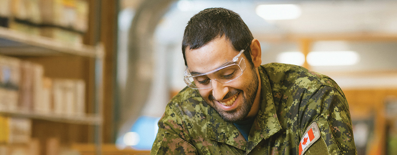 A person wearing a military uniform, smiling in a trades shop.