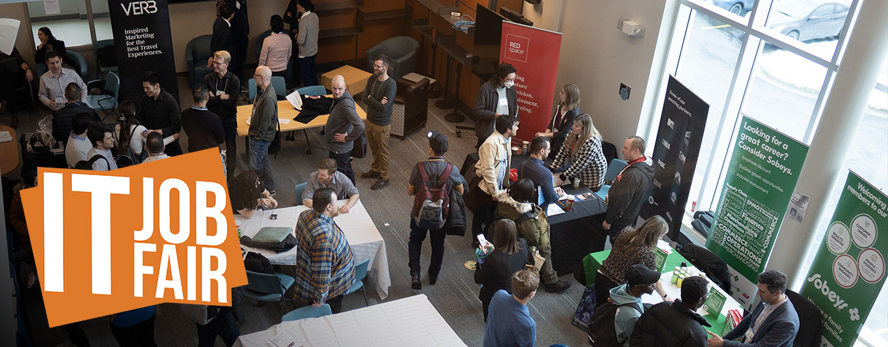 An overhead view of the Information Technology Job Fair event taking place. A crowd of attendees moves within the space. Information booths with pull up banners from a variety of businesses are set up throughout the room. A designed text logo with an orange background and white font is in the bottom left corner of the image reads as: IT Job Fair