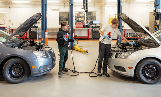 Two youth standing in front of vehicles holding cables