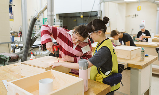 A youth working on a carpentry project while a youth leader stands next to her