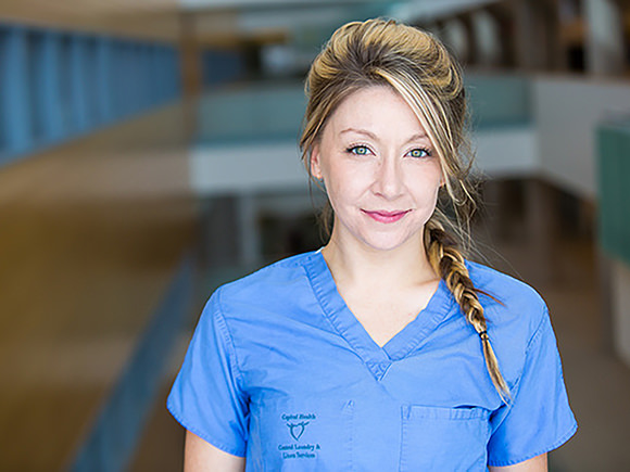 A woman in a blue shirt with a braid in her hair looks straight ahead and smiles against an out-of-focus background.