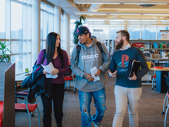 A group of four students study together with books open at a round table in a library.