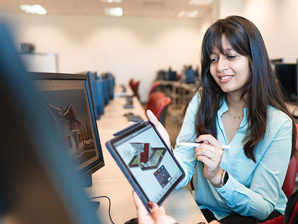 Two female students look at renderings on their computer screens.