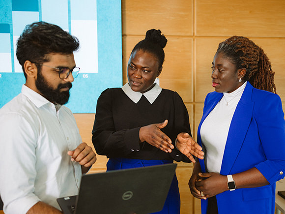 A Business Analysis grad talks to other students in the program while looking at a laptop together.