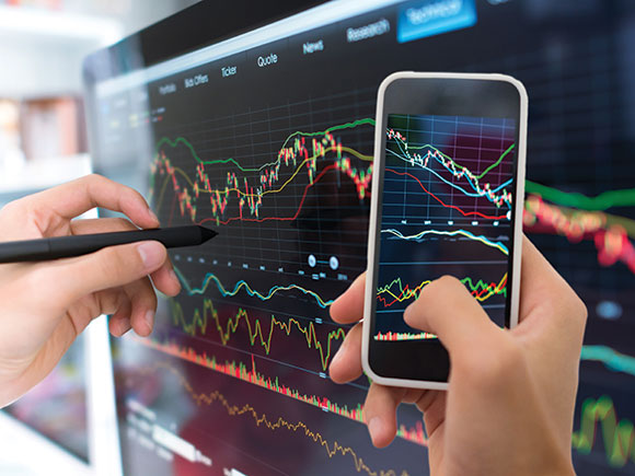 A close-up photo of a hand drawing graphs and charts on a tablet screen and another hand holding a smartphone.