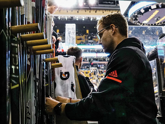 A person wearing glasses and a hoodie arranges hockey equipment inside an arena.