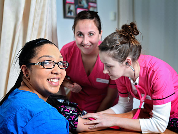 Three Continuing Care Assistant students practise hands-on learning in a clinical setting.