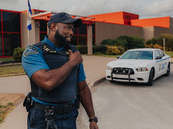 A man in a sheriff's uniform talks into a shoulder walkie talkie while standing in front of a stone building.