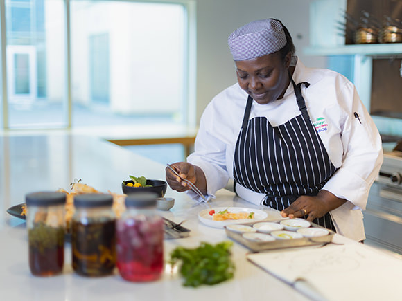 A woman in chef's hat, and apron works on a culinary delight.