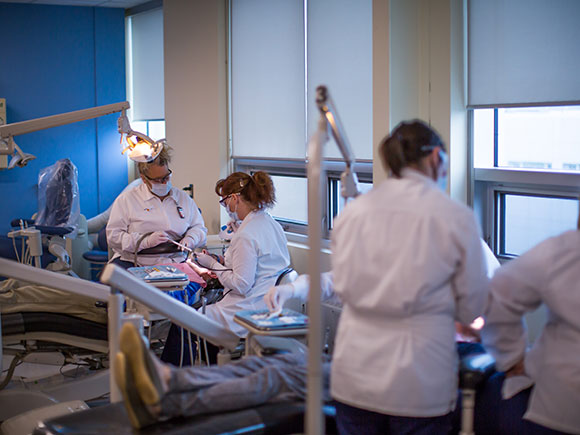 A group of students wearing lab coats practice dental skills in a lab.