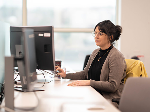 A woman in glasses sits working at her computer.