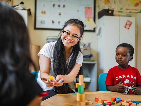 An Early Childhood Educator sits at a small table with a young child.