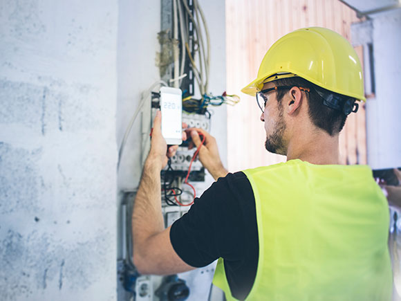 A man in a yellow hard hat, vest and safety googles uses equipment on the job.