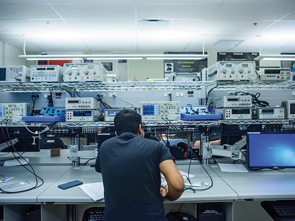 A man sits at a desk and works on electronic equipment in a campus learning lab setting.