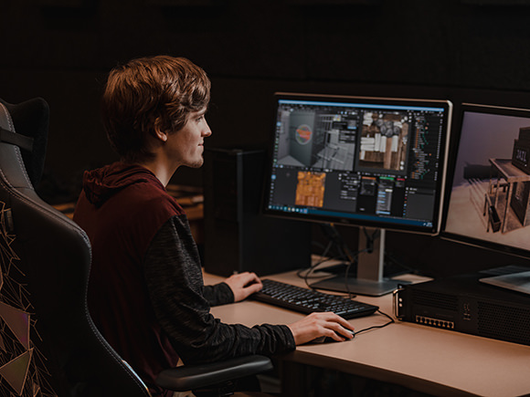 A student sits in front of multiple monitors.