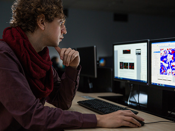 A man sits in front of multiple monitors displaying geographic information data.