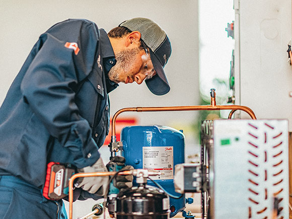 A man, holding a tool in his hand, works on a mechanical system.