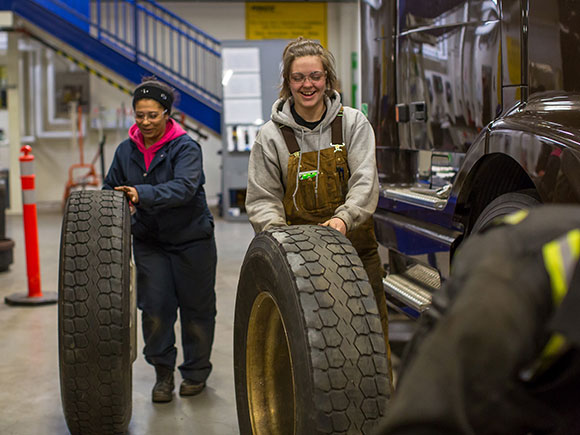 Two students in overalls roll large tires in NSCC's heavy duty equipment shop.