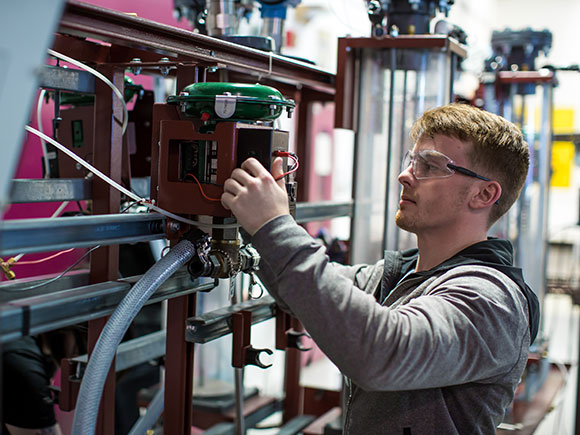 A man in protective eye goggles works on a piece of equipment.