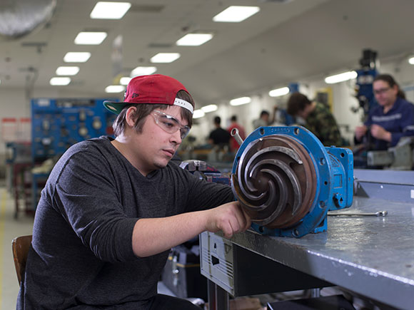 A man in protective eye goggles works on a small piece of mechanical equipment.