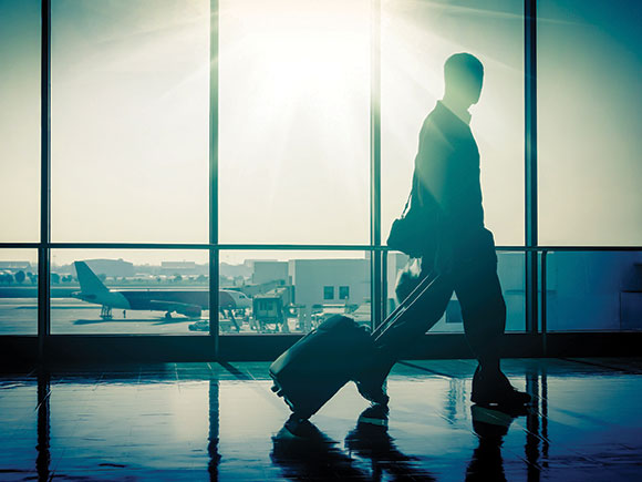 A businessman pulls a carry-on suitcase through an airport terminal.