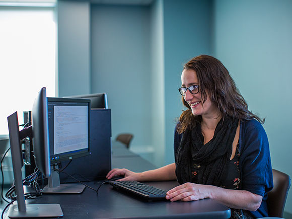 A woman sits at her desk smiling and looking at her computer screen.