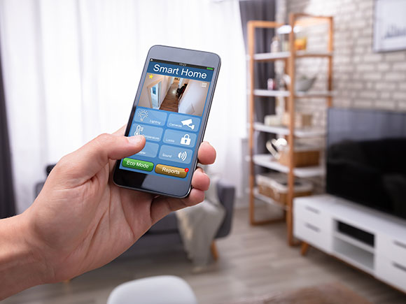 A hand is shown holding a cell phone inside a living room. The phone's screen displays the words smart home.