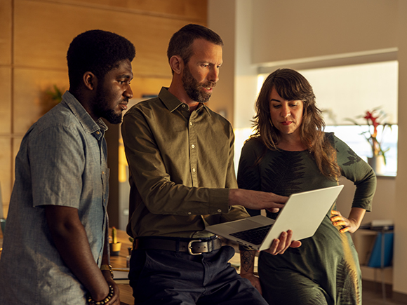 Two men and one woman look at a laptop computer together.