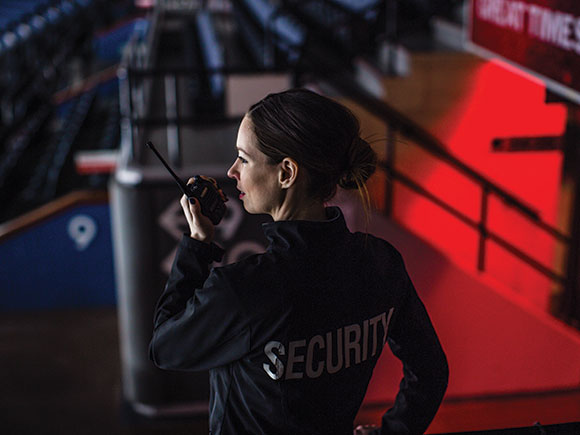A woman in a security uniform talks on a two-way radio.