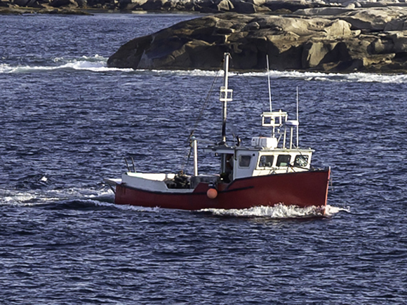 A small red fishing boat sails along the coastline.