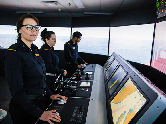 Three students in uniform practise their skills inside the Nautical Institute's marine navigation simulator.