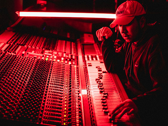 A man sits at a sound board; the room is lit with a red glow.